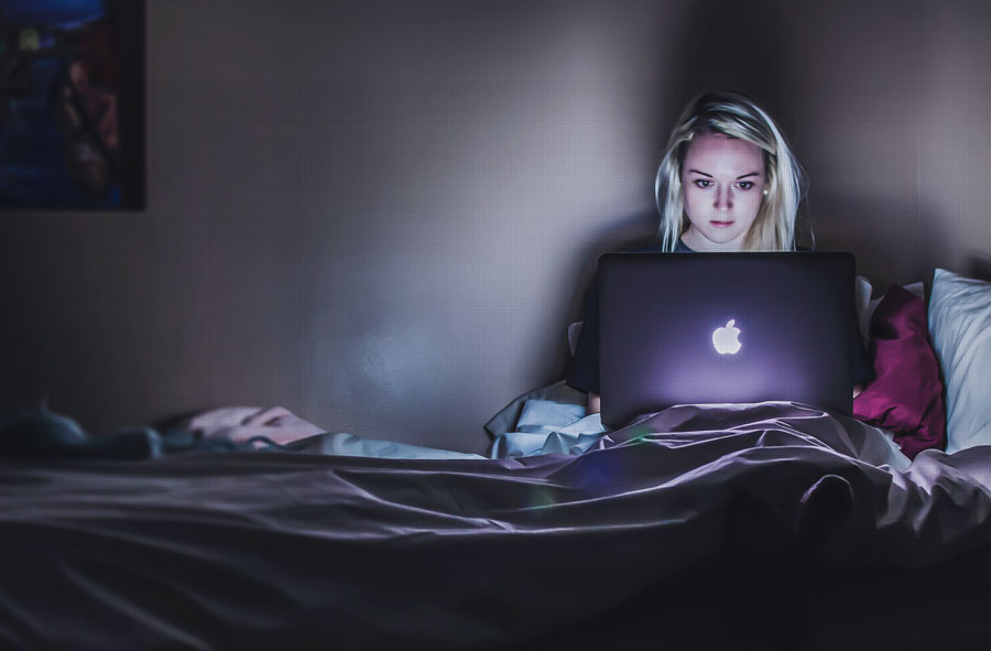 Woman sitting on bed and working on a laptop.