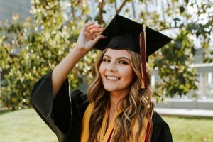 Smiling female PhD graduate in cap and gown adjusting her tassel outdoors, representing success, confidence, and the completion of an academic journey.
