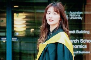 Young woman in academic graduation gown standing in front of the Australian National University.